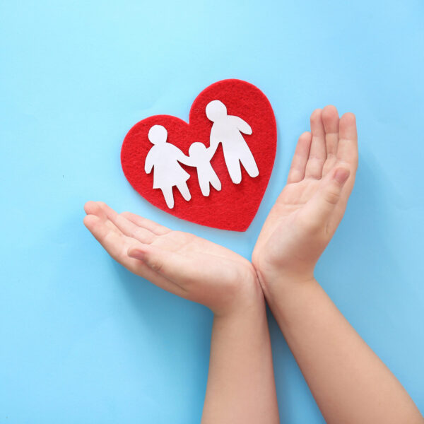 Child protecting red heart with paper silhouette of people on color background, top view